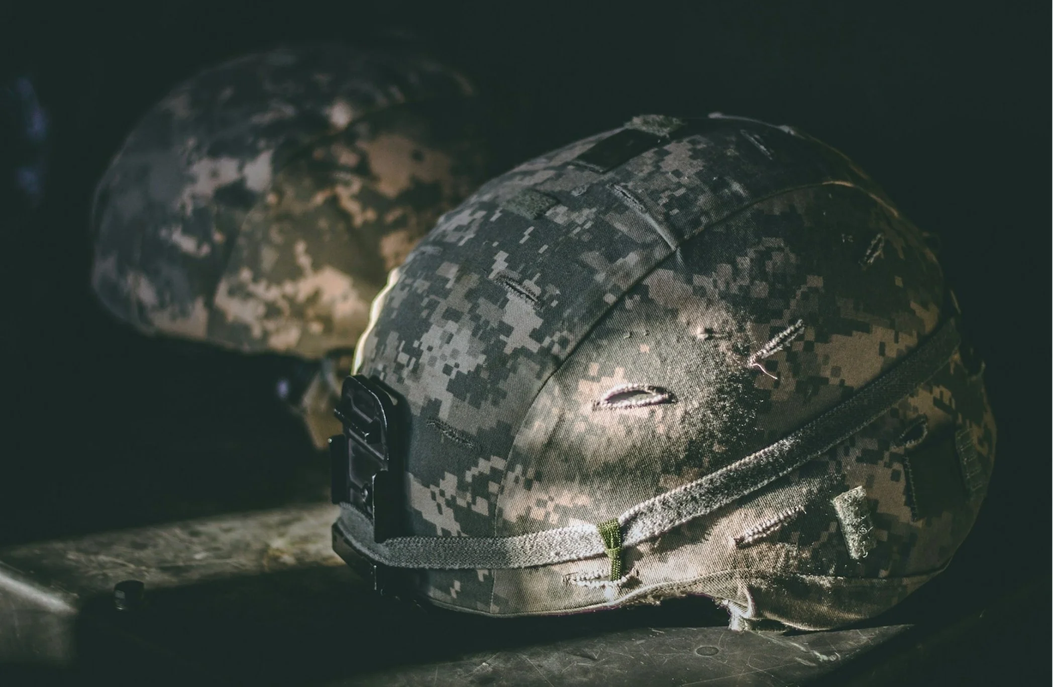 Close-up of military camouflage helmet and backpack on dark surface.