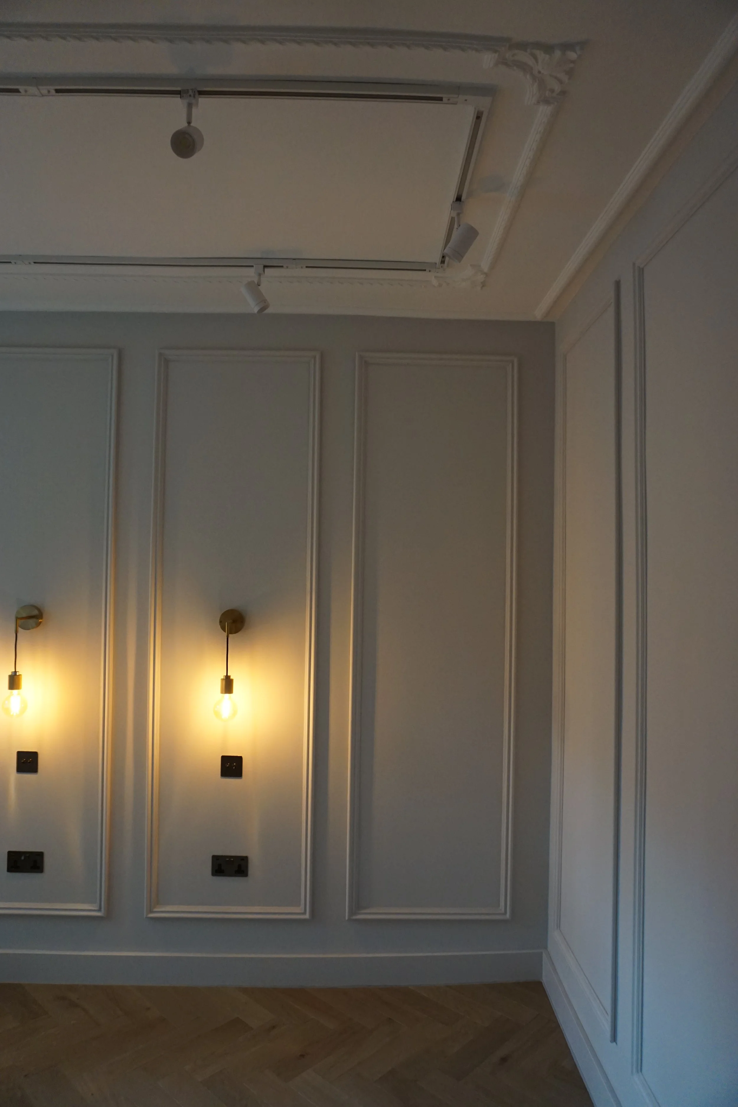 Interior wall with decorative molding, two wall-mounted light fixtures, and multiple electrical outlets.