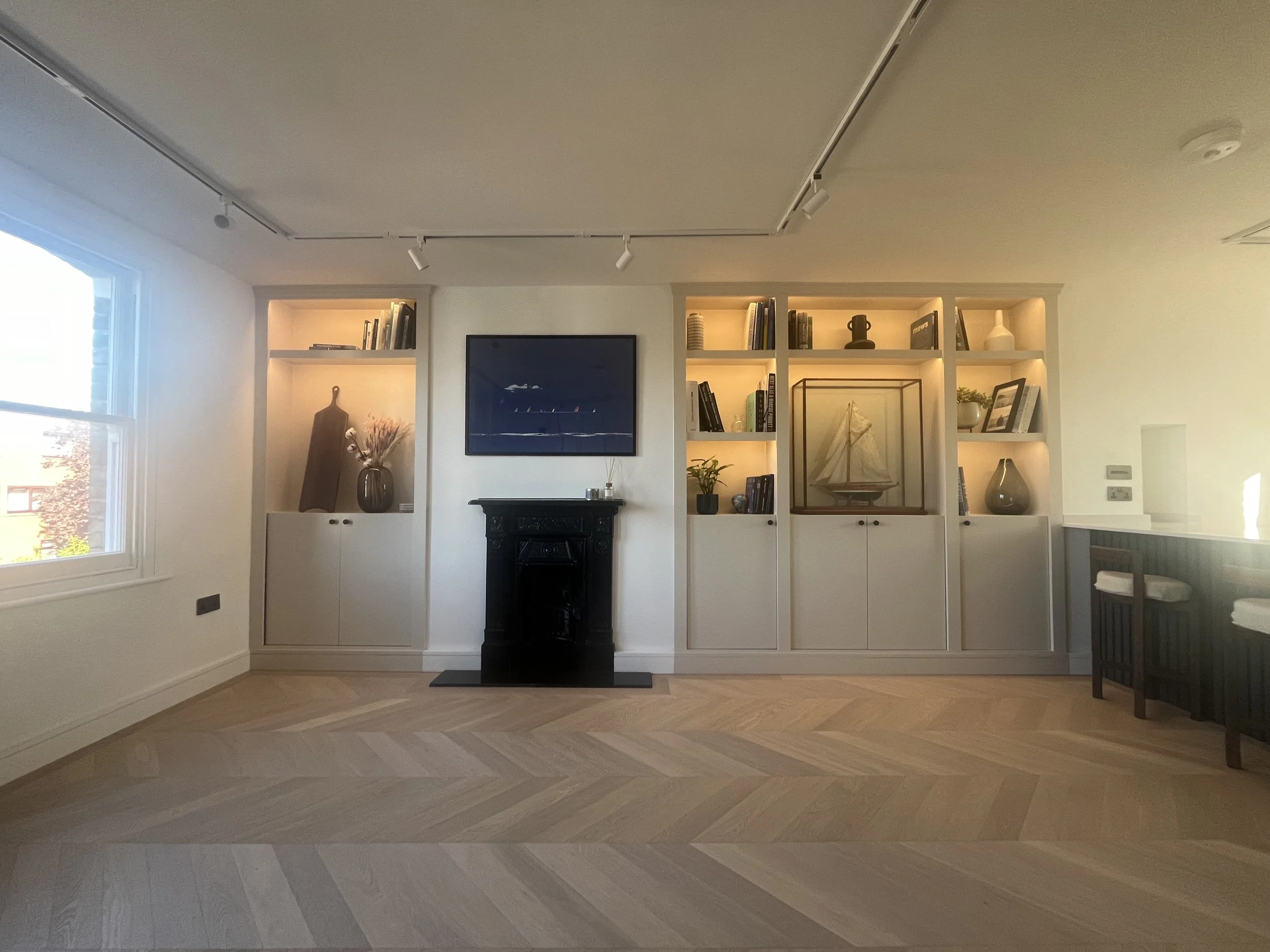 Living room with white built-in shelves, a black fireplace mantel, a vase with flowers, a television mounted on the wall, and decorative items like a model sailboat and framed pictures.