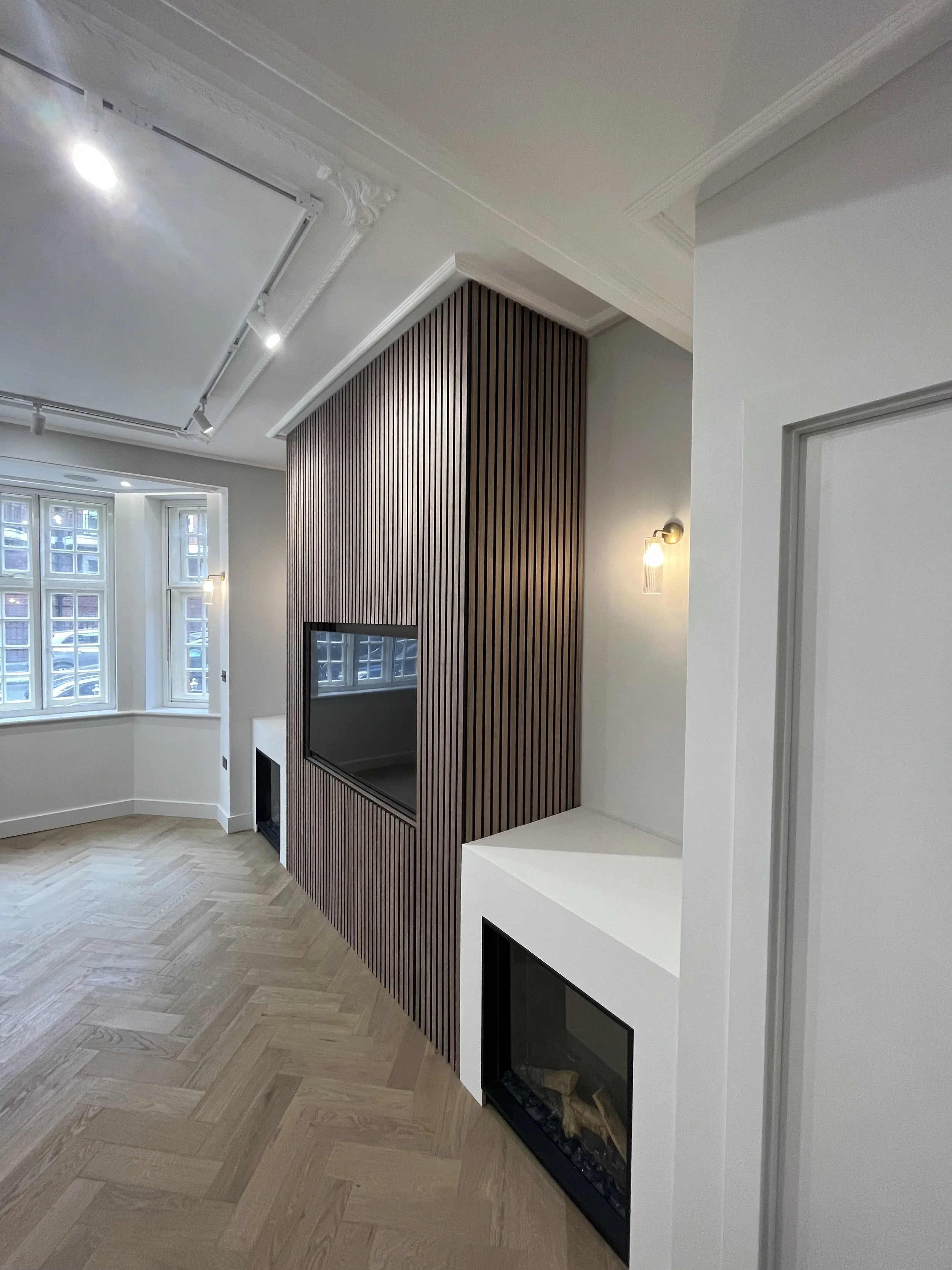 A modern living room with white walls, a fireplace, wooden paneling, and large windows with white curtains.