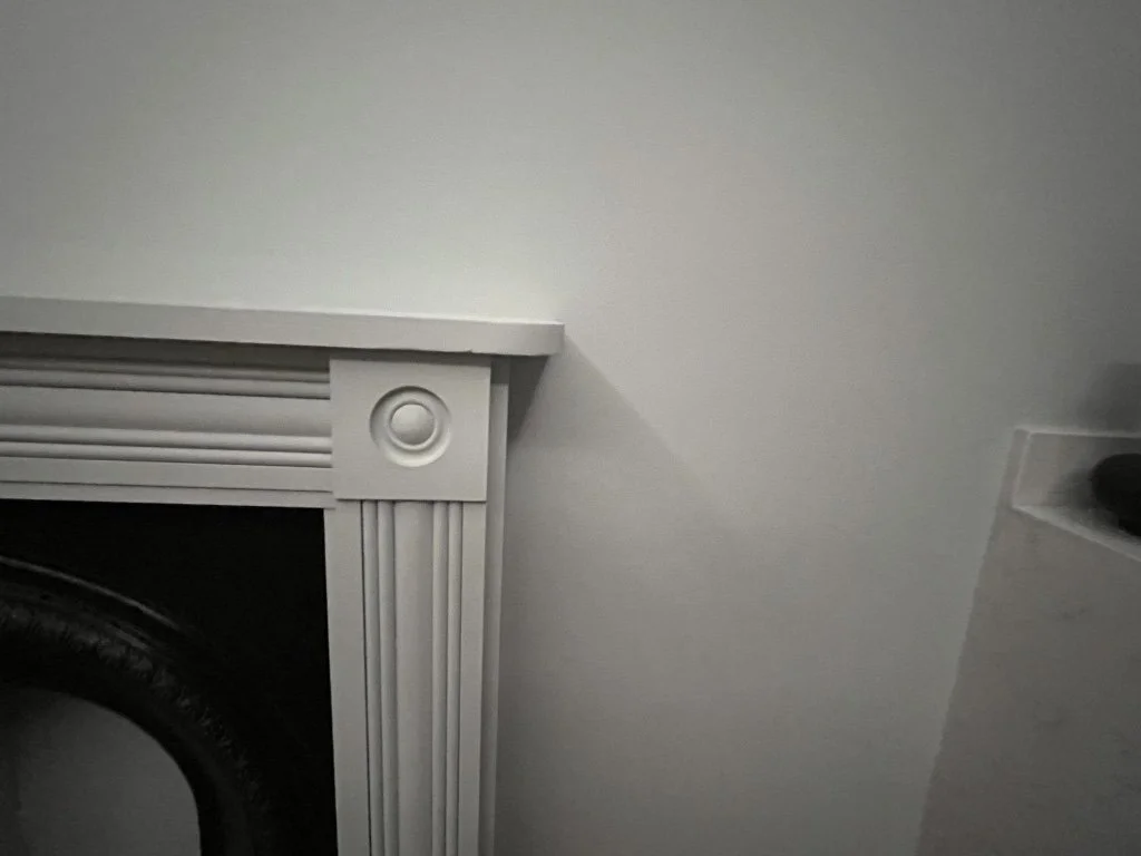 Close-up of a white fireplace mantel with decorative molding, against a beige wall.