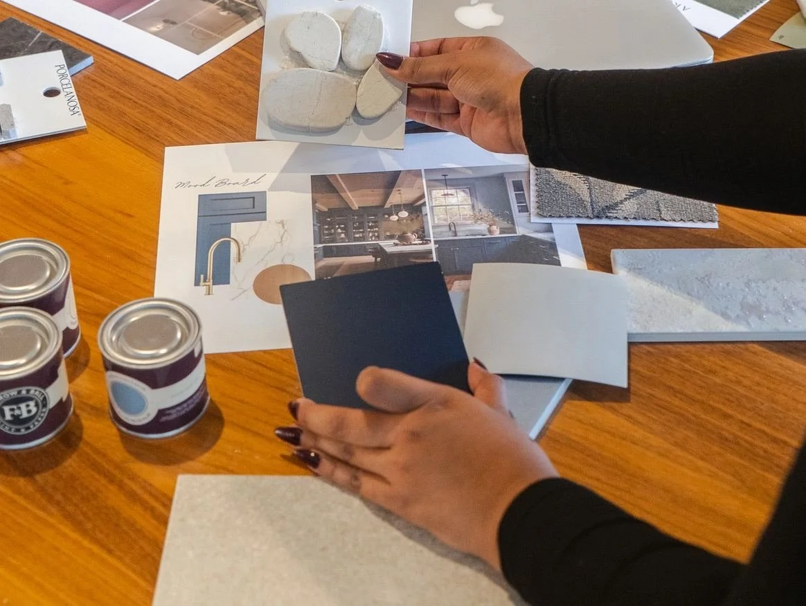 Person examining samples of paint chips and interior design inspiration boards on a wooden table for a kitchen renovation project.