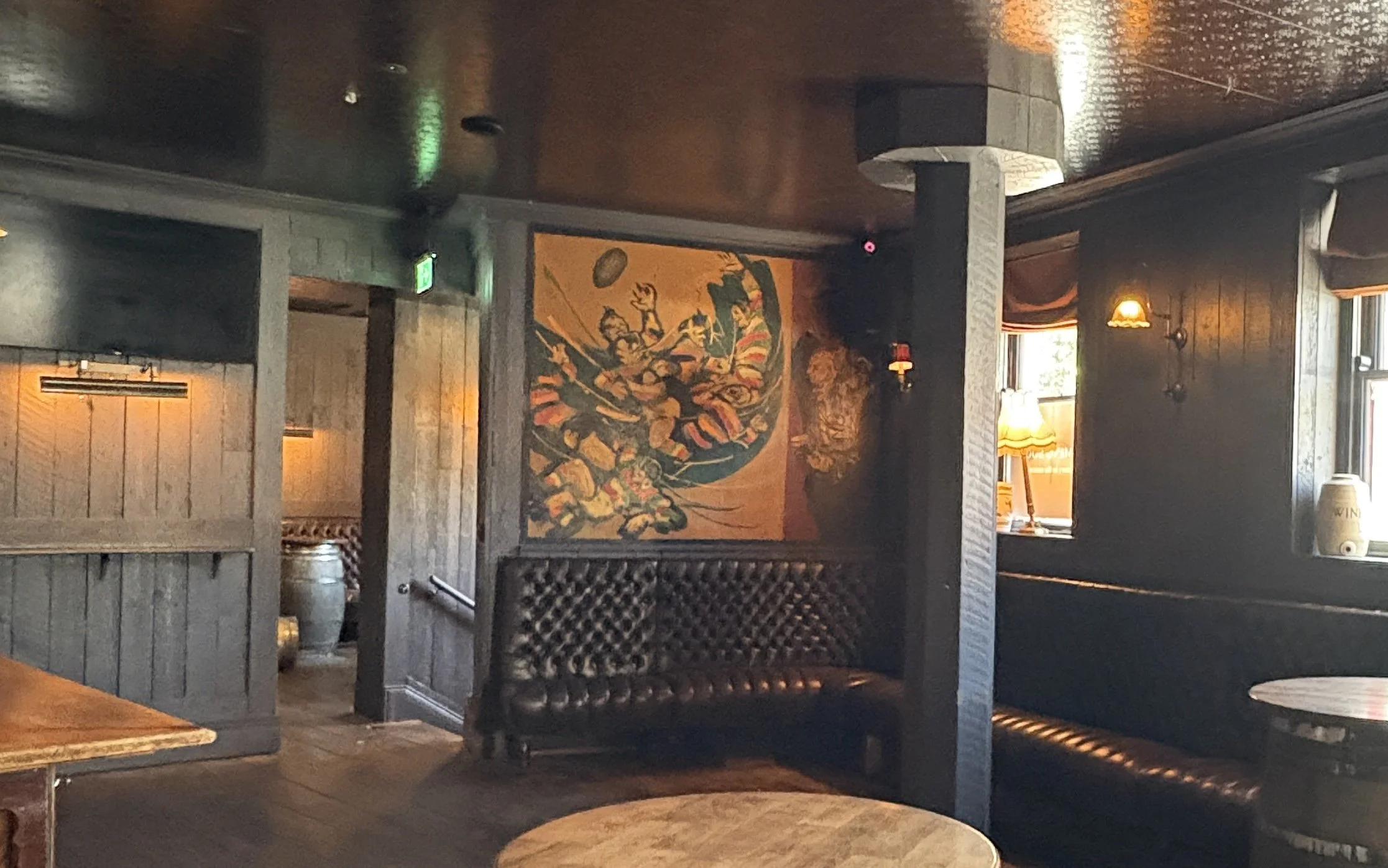 Interior of a restaurant or pub with dark wooden walls, a vintage painting, and cozy lighting fixtures. This unique rugby mural was painted in the 1960s by Owen Walsh, one of Ireland's most distinctive modern artists, who lived on Baggot Street.