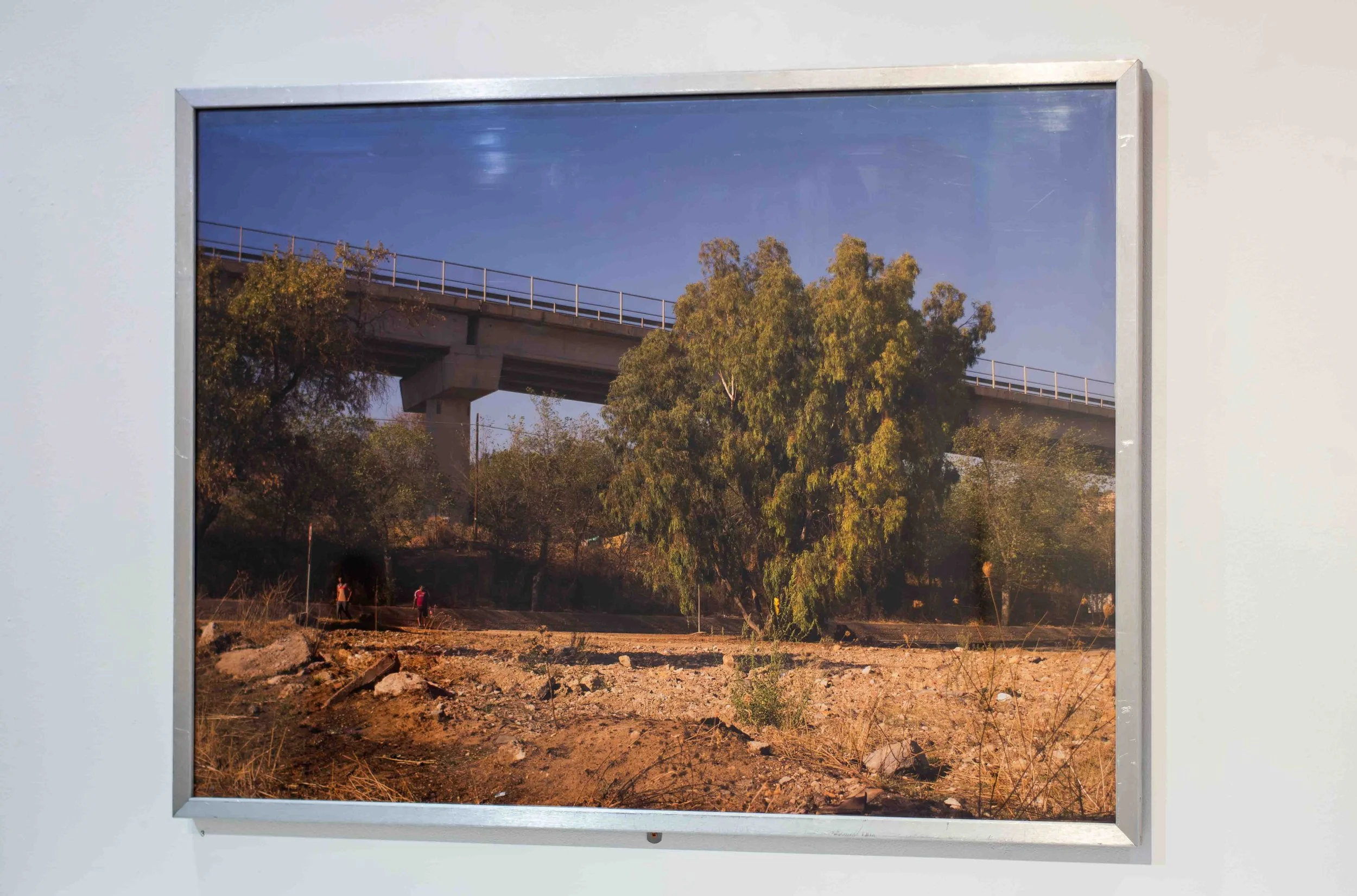 Photograph of a mural depicting a highway overpass, trees, and a blue sky, framed in white.