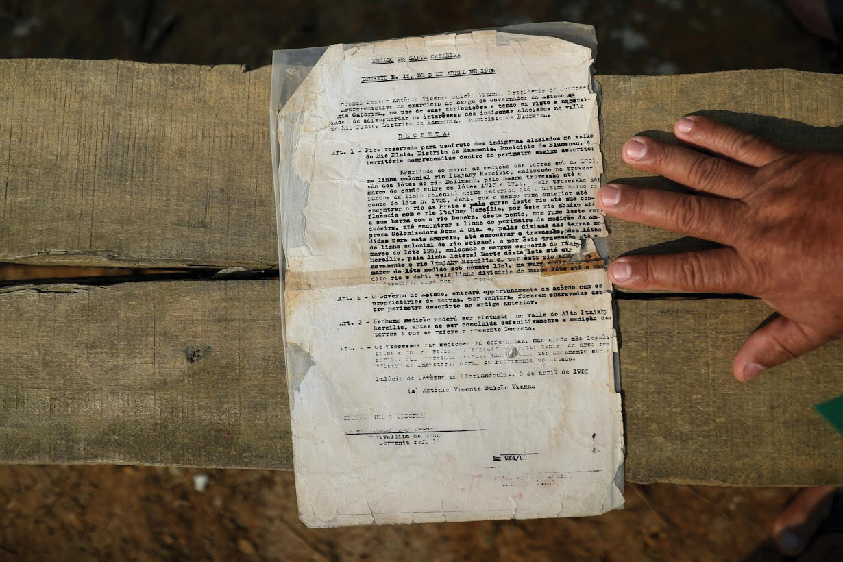 A worn and torn official document with typed text in Spanish, placed on a wooden surface, with a person's hand holding the edge on the right side.