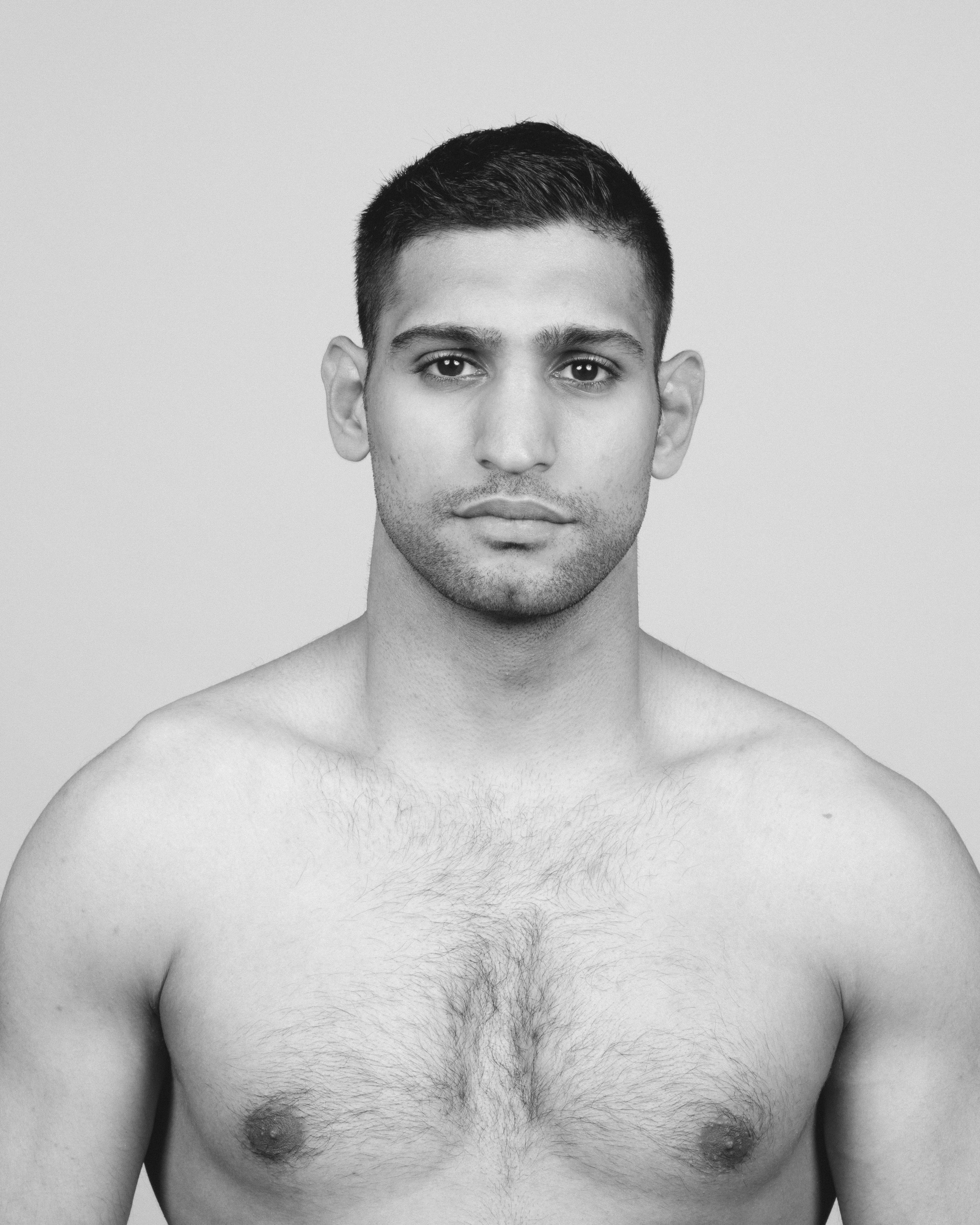 Black and white photo of a shirtless man with short dark hair, looking directly at the camera with a neutral expression.