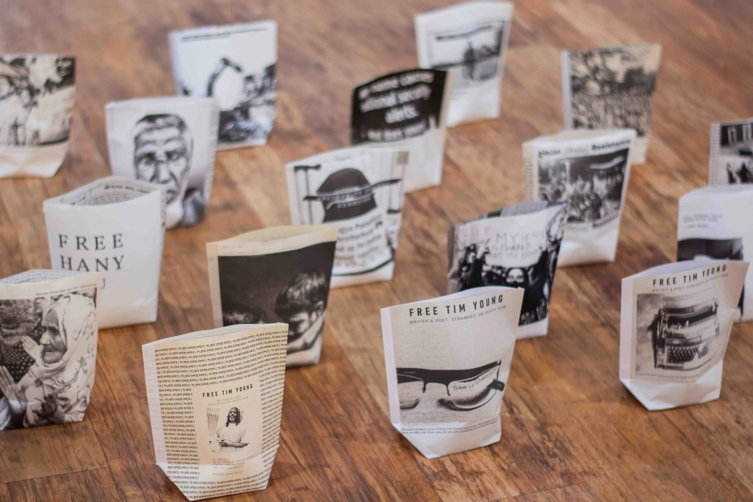 Multiple folded flyers or posters laid out on a wooden floor, with some text and black and white images visible on them.