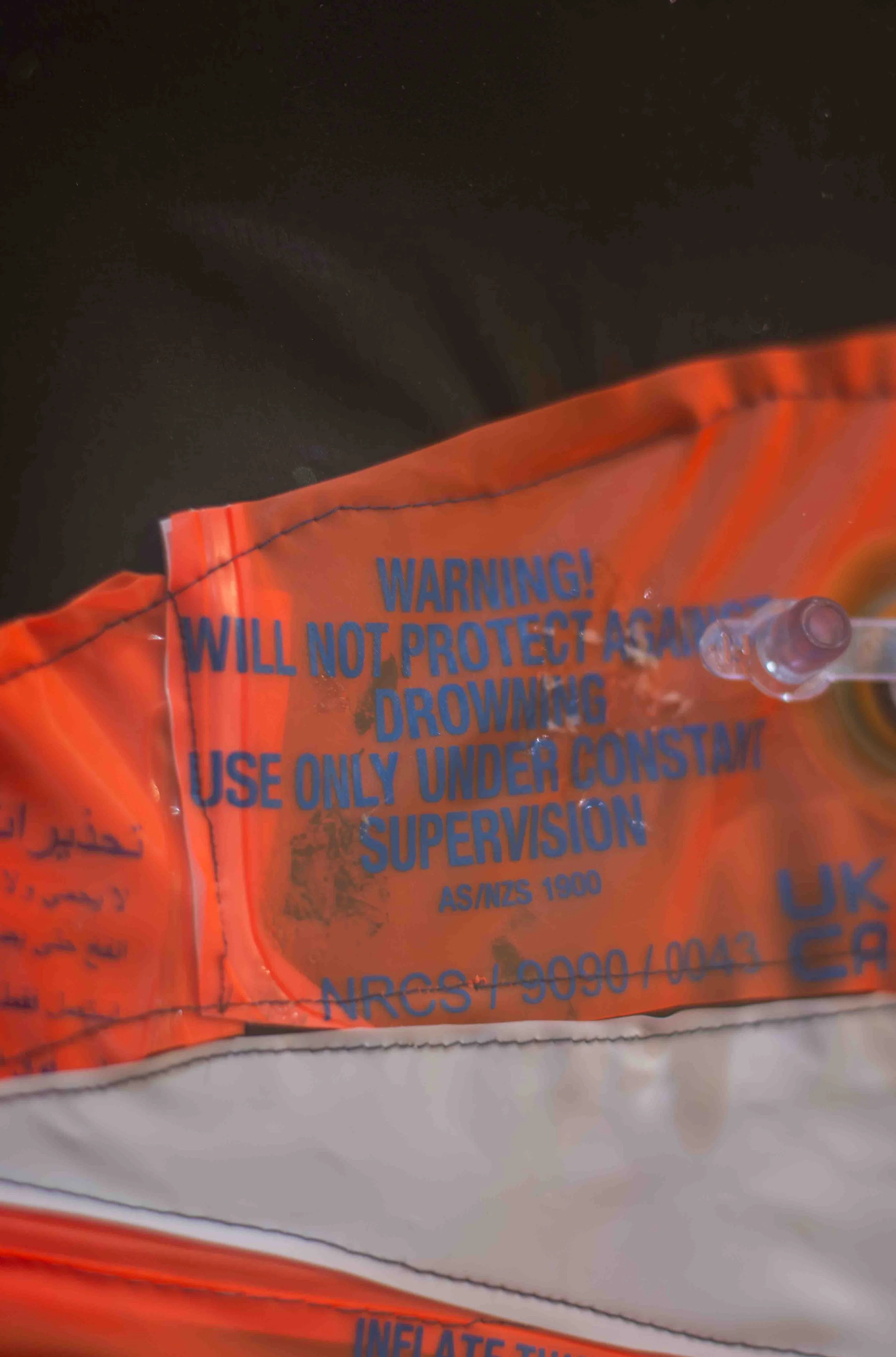 Close-up of an orange safety device with blue text warning that it will not protect against drowning, and indicates it should be used only under supervision.