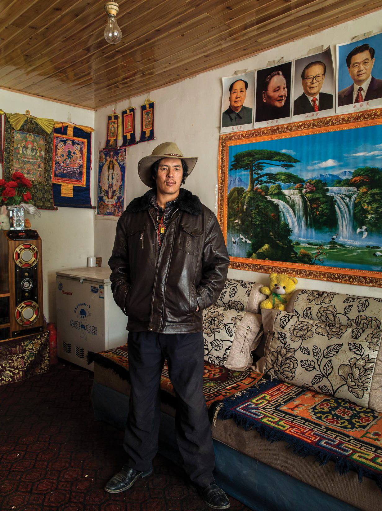 A man standing in a room decorated with posters, artwork, and textiles, wearing a cowboy hat and leather jacket.