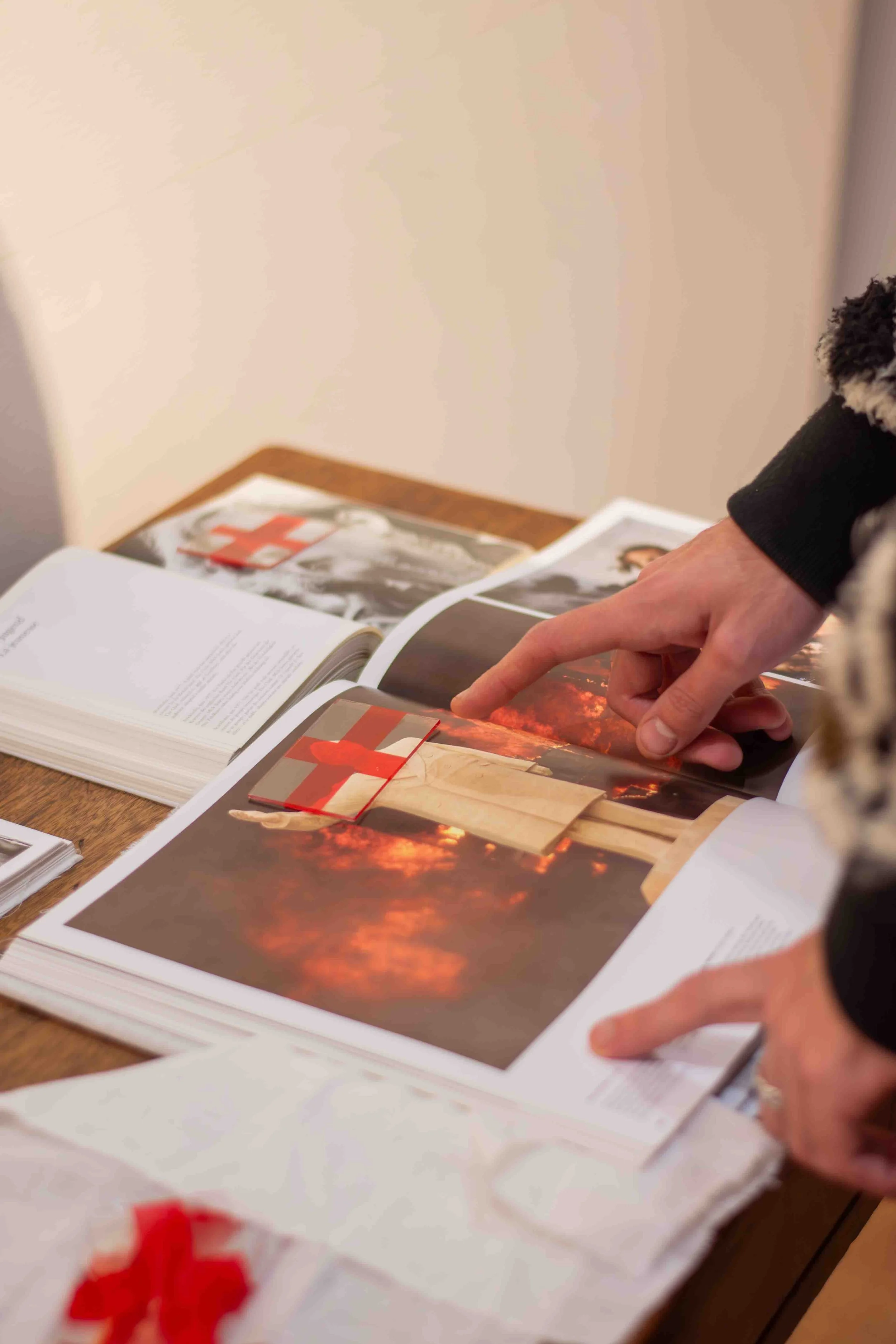 Close-up of a person pointing at pages in an open book with photographs and text, on a wooden table.