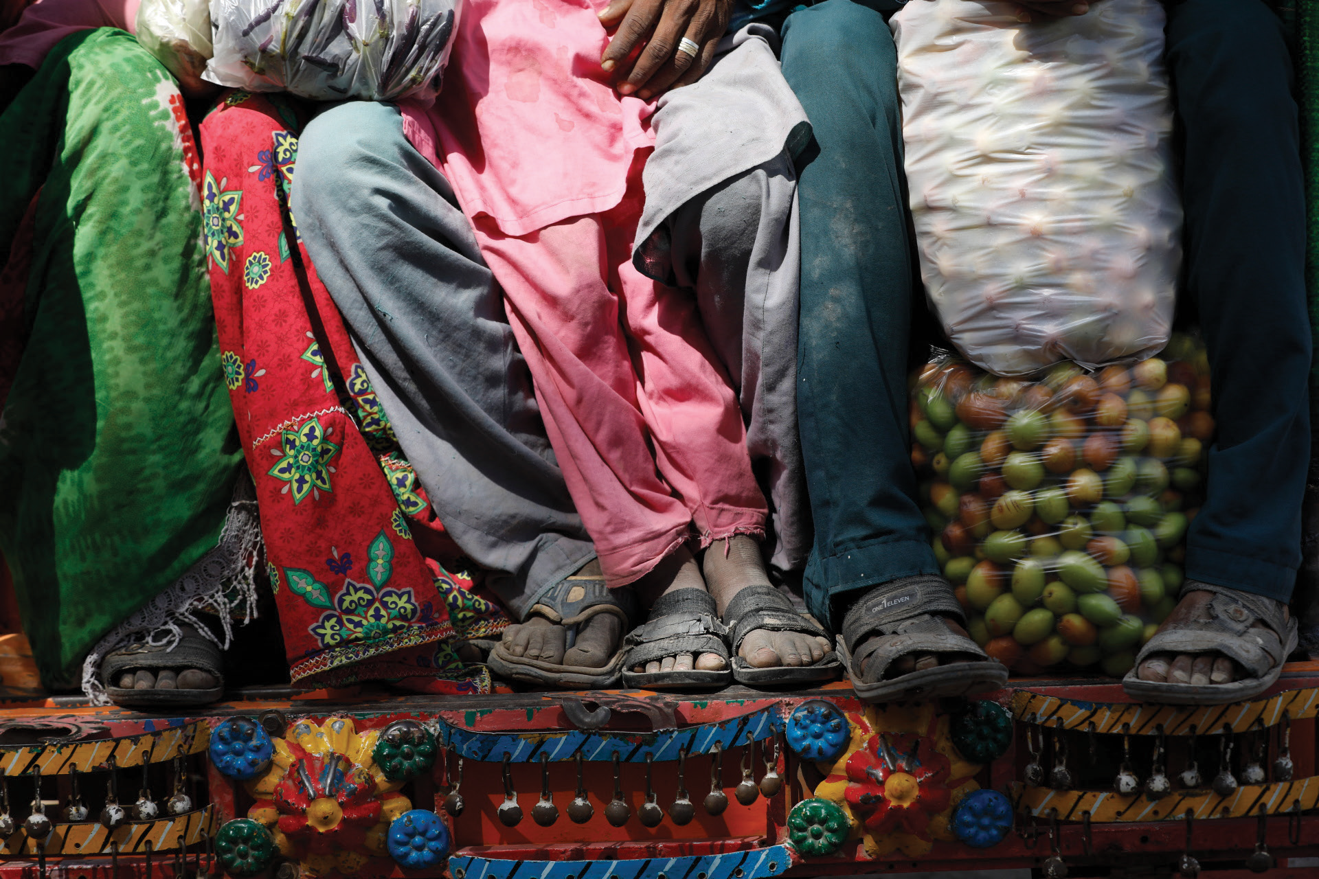 Close-up of people's feet standing on a colorful, decorated platform with various fabrics and a bag of onions next to them.