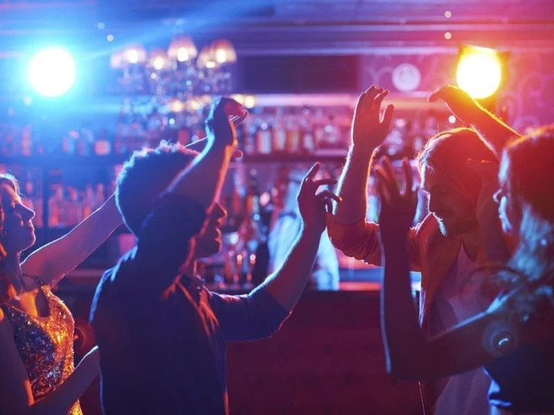 People dancing and enjoying music at a nightclub with colourful lights.
