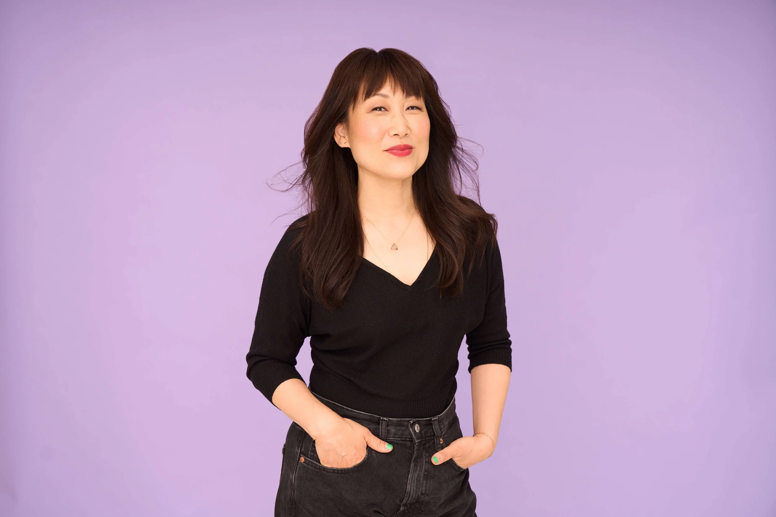 Hannah Sung standing against a light purple background, smiling with one hand in her pocket.