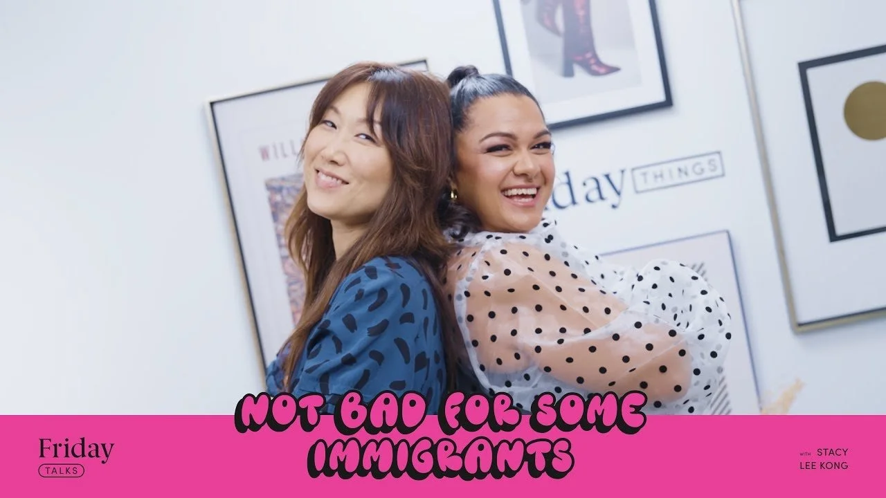 Hannah Sung and Stacy Lee Kong smiling and leaning against each other, standing in front of a wall with framed pictures and text.