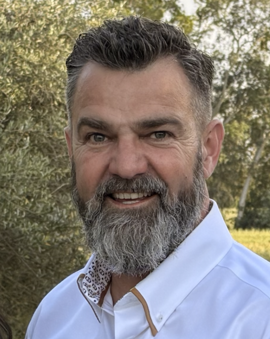 Close-up of a middle-aged man with a beard and short dark hair, smiling outdoors with trees in the background, wearing a white collared shirt. This is Menno Koehoorn, CEO and founder of TechMist Spray Solutions.