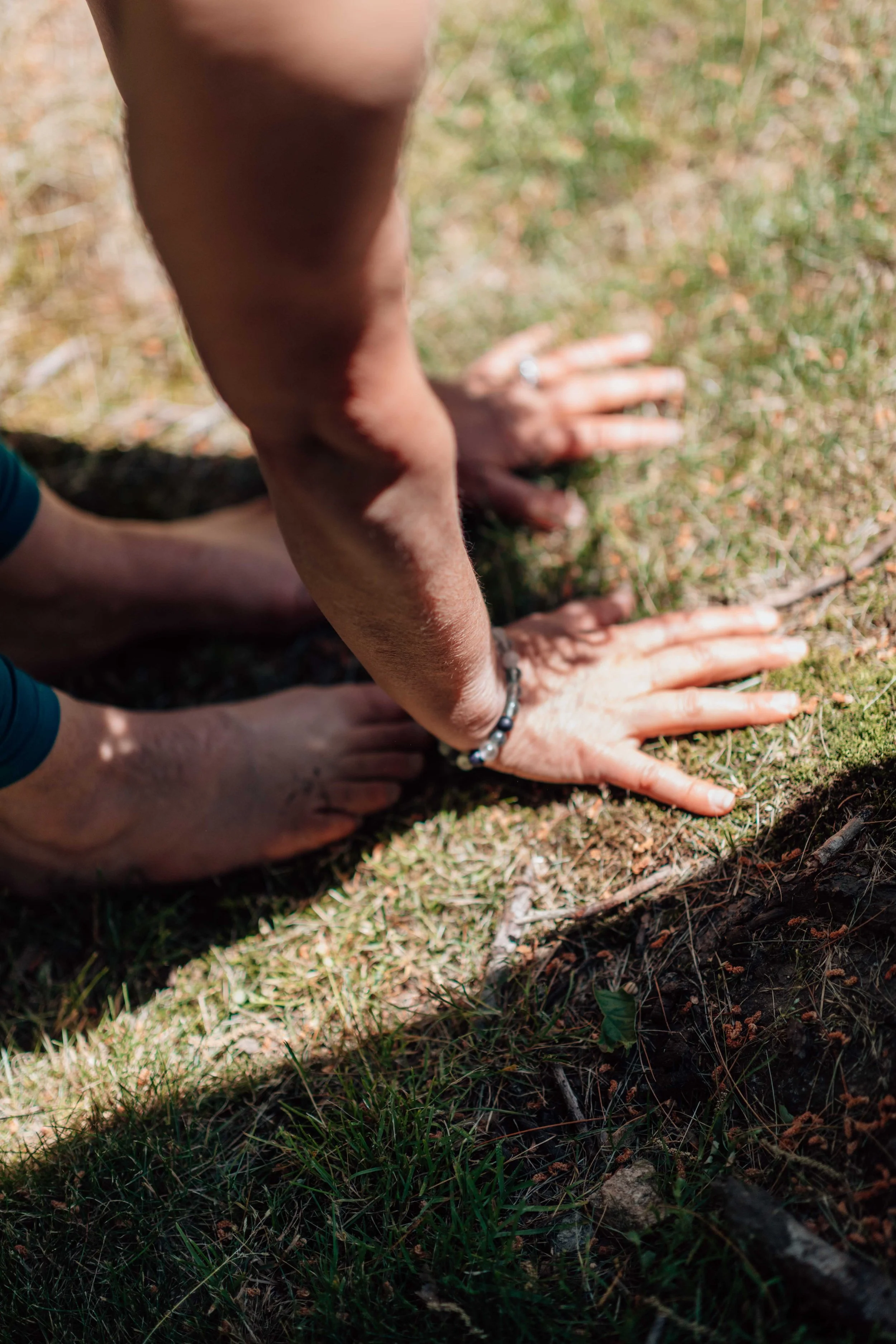 Two human hands on the ground with dirt, grass, and small twigs, positioned in a crawling or starting stance outdoors.