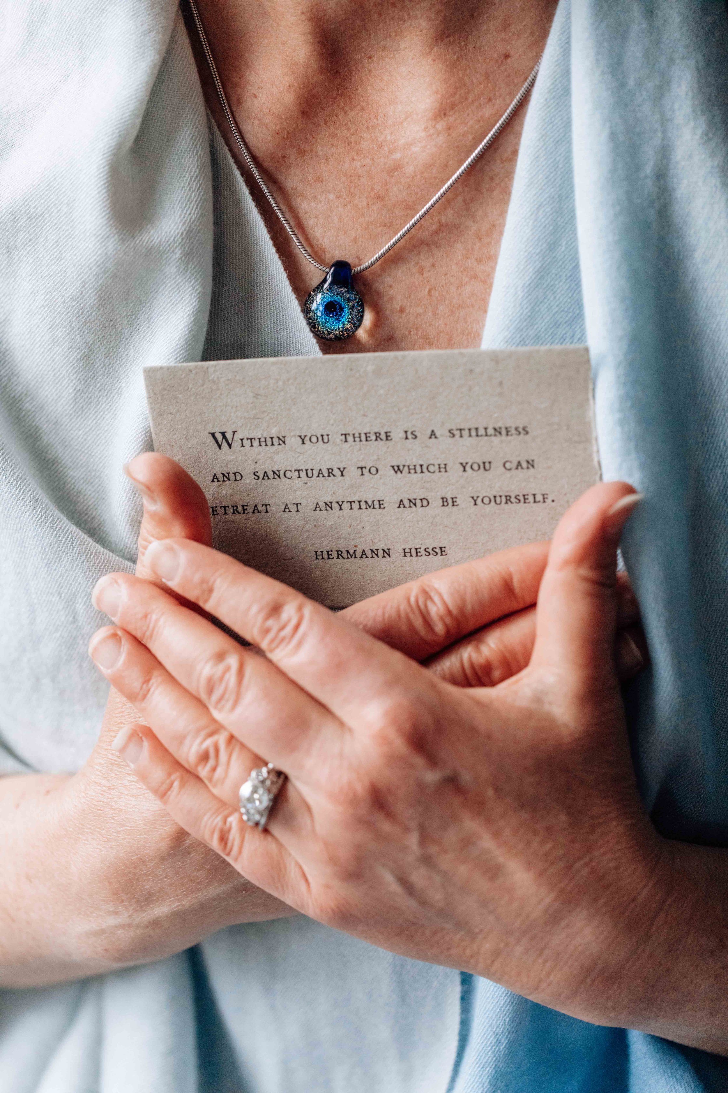 Person holding a note with an inspirational quote, wearing a necklace with a blue eye pendant, and a silver ring with a large gemstone.