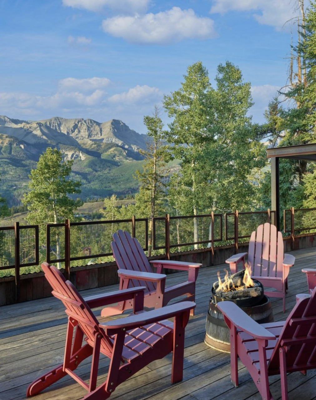 Outdoor deck with pink Adirondack chairs surrounding a fire pit, overlooking a mountain range and lush green trees. | South Denver residential home in the Denver metro area