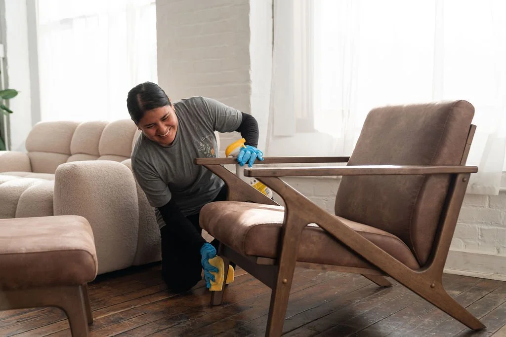 A woman cleaning a mid-century modern armchair inside a living room.