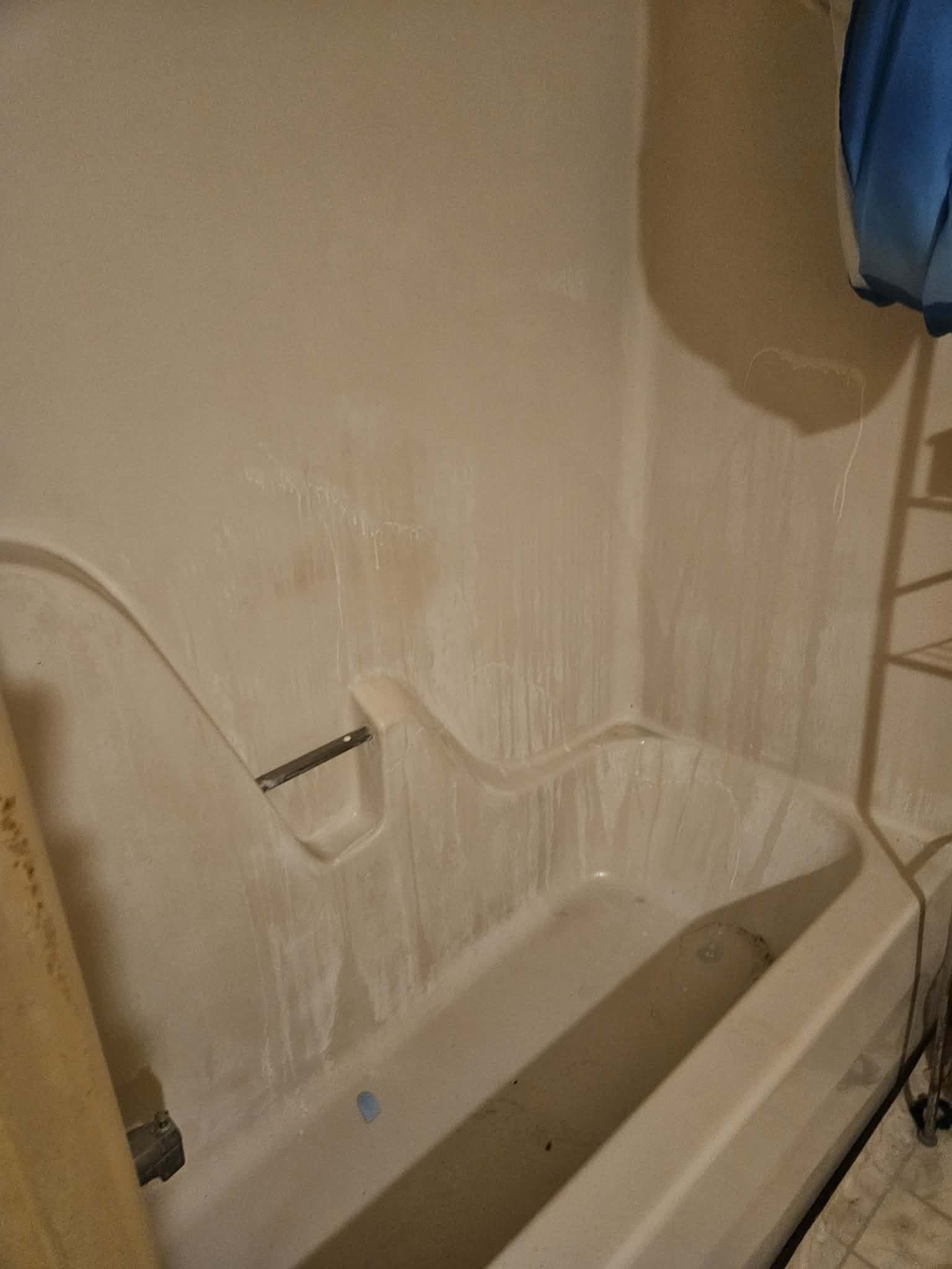 A bathroom shower with a showerhead, soap dish, and shampoo bottle, with a curtain rod at the side.