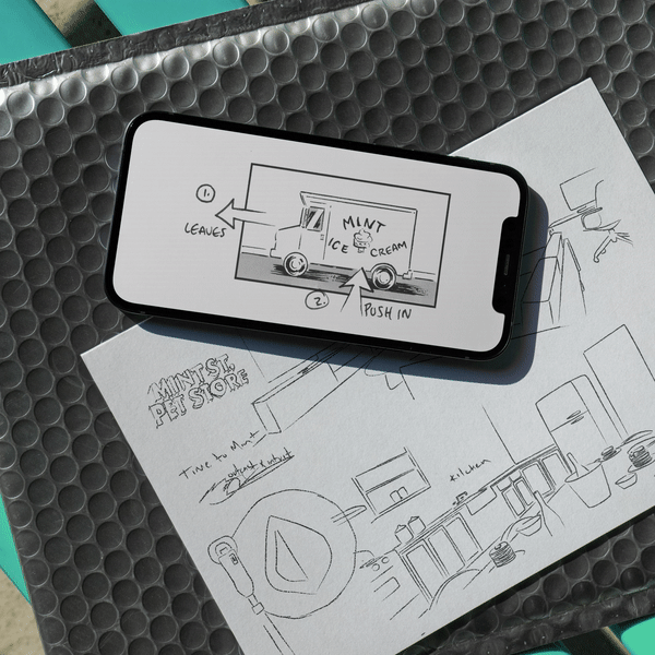 Black and white sketch of a mint ice cream truck on a sheet of paper, with handwritten labels, placed under a smartphone showing the truck's diagram, on textured surface.