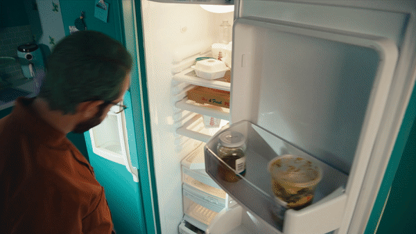 A person looking inside an open refrigerator with drinks and food items on the shelves and door