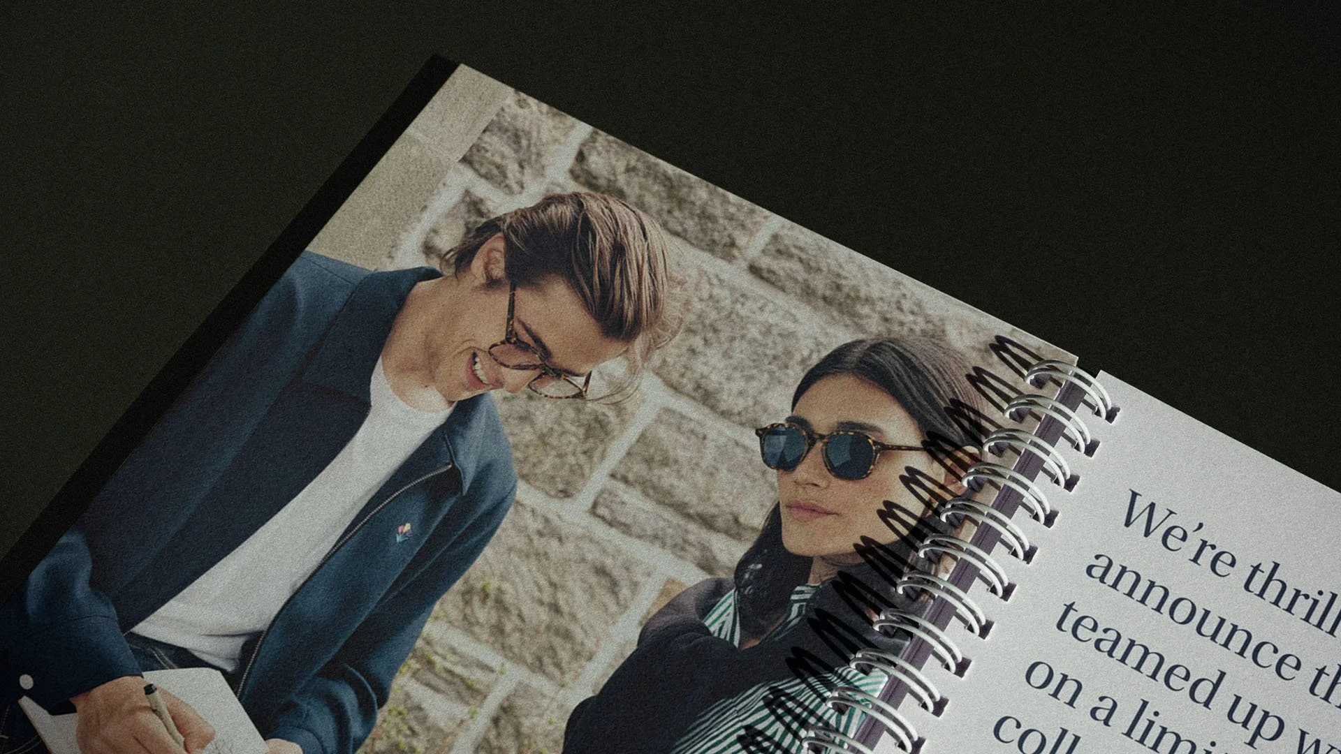 Close-up of a photo of two women with sunglasses, smiling and talking outdoors in front of a brick wall, on a spiral-bound notebook with text.