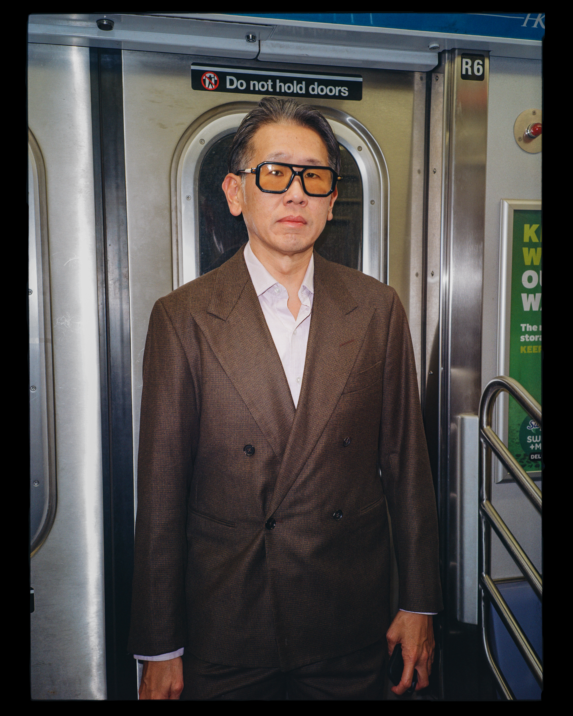 A man in a brown suit and glasses standing in a subway train doorway.