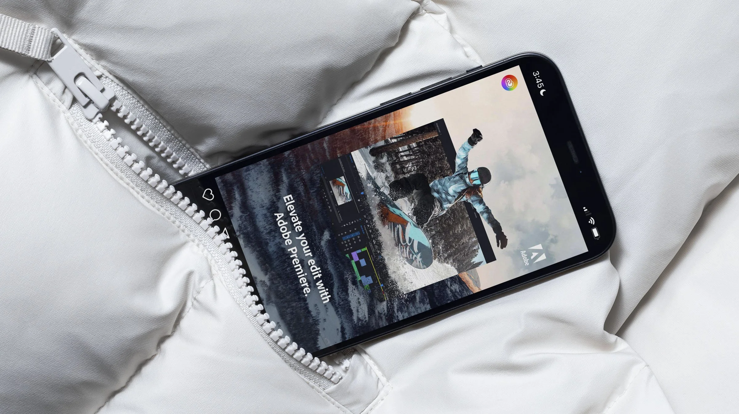 Smartphone lying on a white surface showing Adobe software interface with a person snowboarding in the background.
