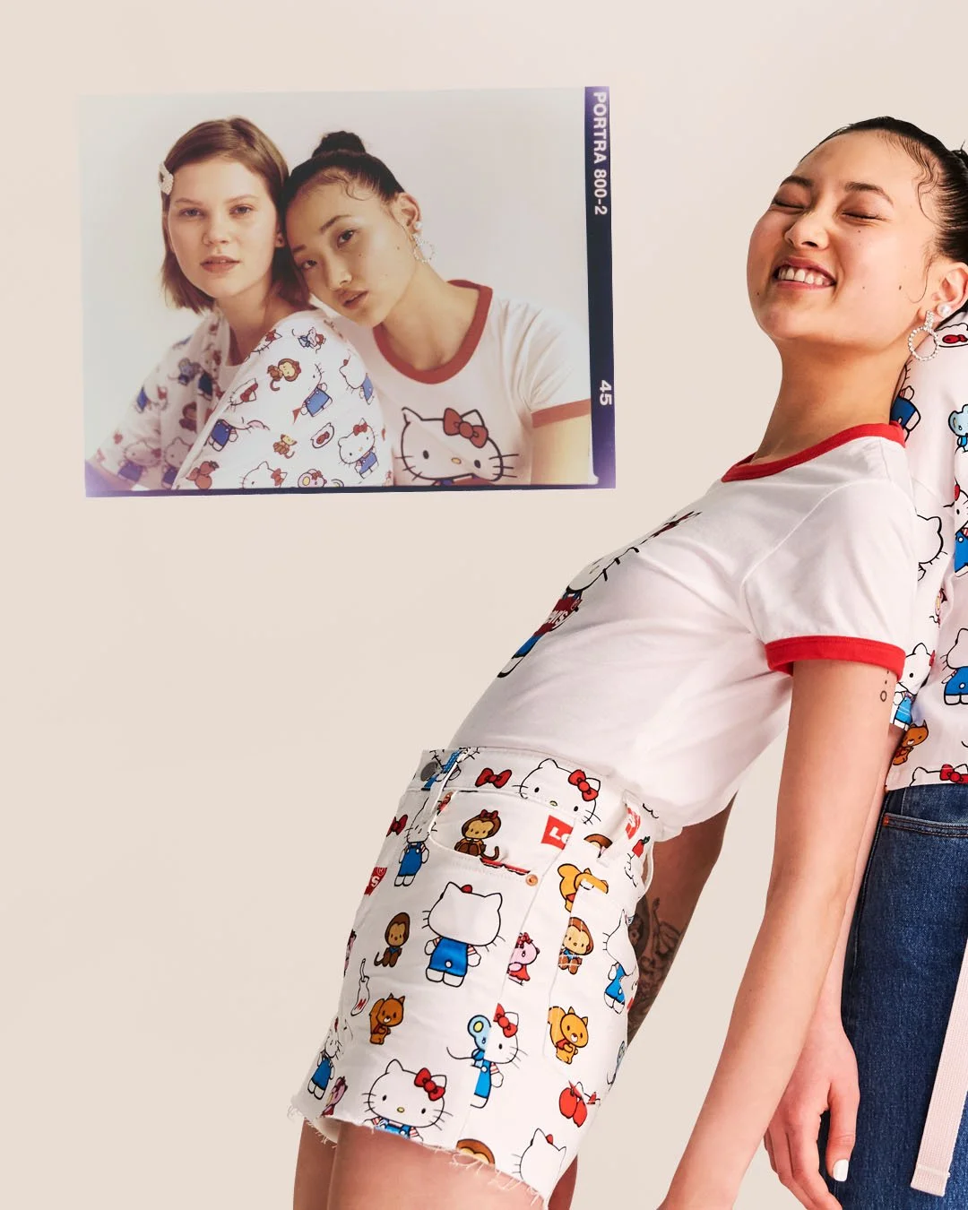 A woman with a big smile and closed eyes wearing a white Hello Kitty shirt and shorts with Hello Kitty and other cartoon character patterns, leaning against a person. A framed photo of two young women with similar Hello Kitty themed clothing is on the wall behind her.