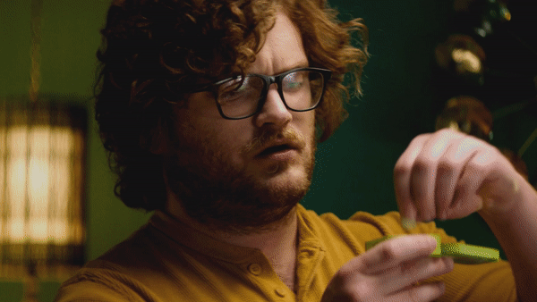 A man with curly hair and glasses opening a bottle of pills.