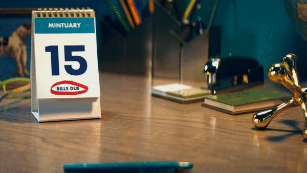 Desk with calendar showing the date 15 and bills due note, pens, notebooks, and decorative items.