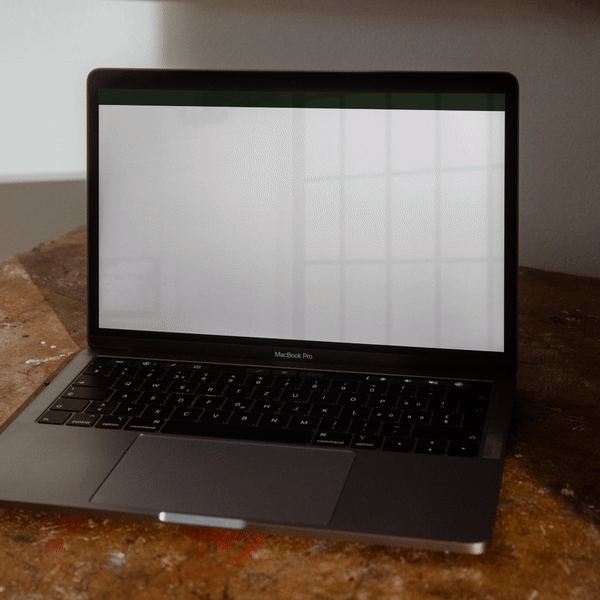 A MacBook Pro laptop with its screen turned on, displaying a blank white background, placed on a wooden table.