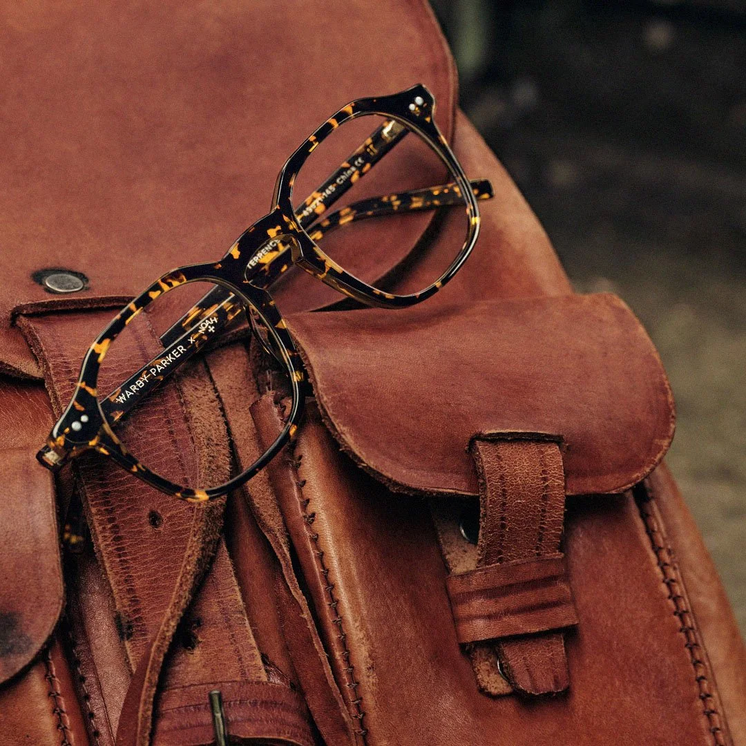 A pair of black and tortoise-shell patterned eyeglasses resting on a brown leather satchel.