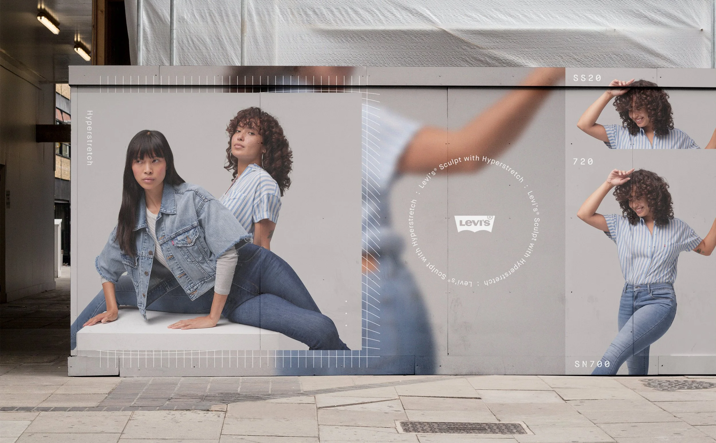 A large advertisement display featuring two women in casual denim outfits, with one crouching on the ground and the other standing with a hand on her hip, set against a plain backdrop with text and logo.