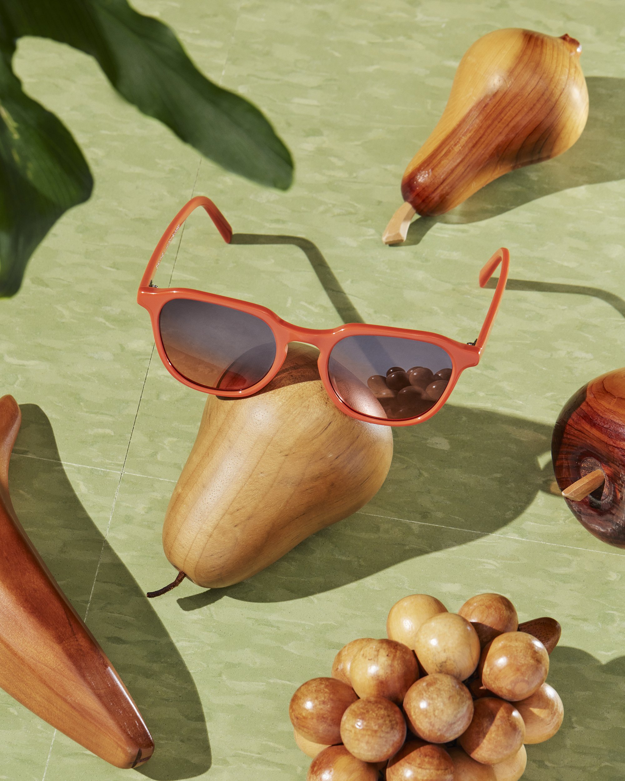 A pair of orange sunglasses with dark lenses, a wooden dog figurine, a bunch of wooden balls, and a wooden cone-shaped object on a green tiled surface.