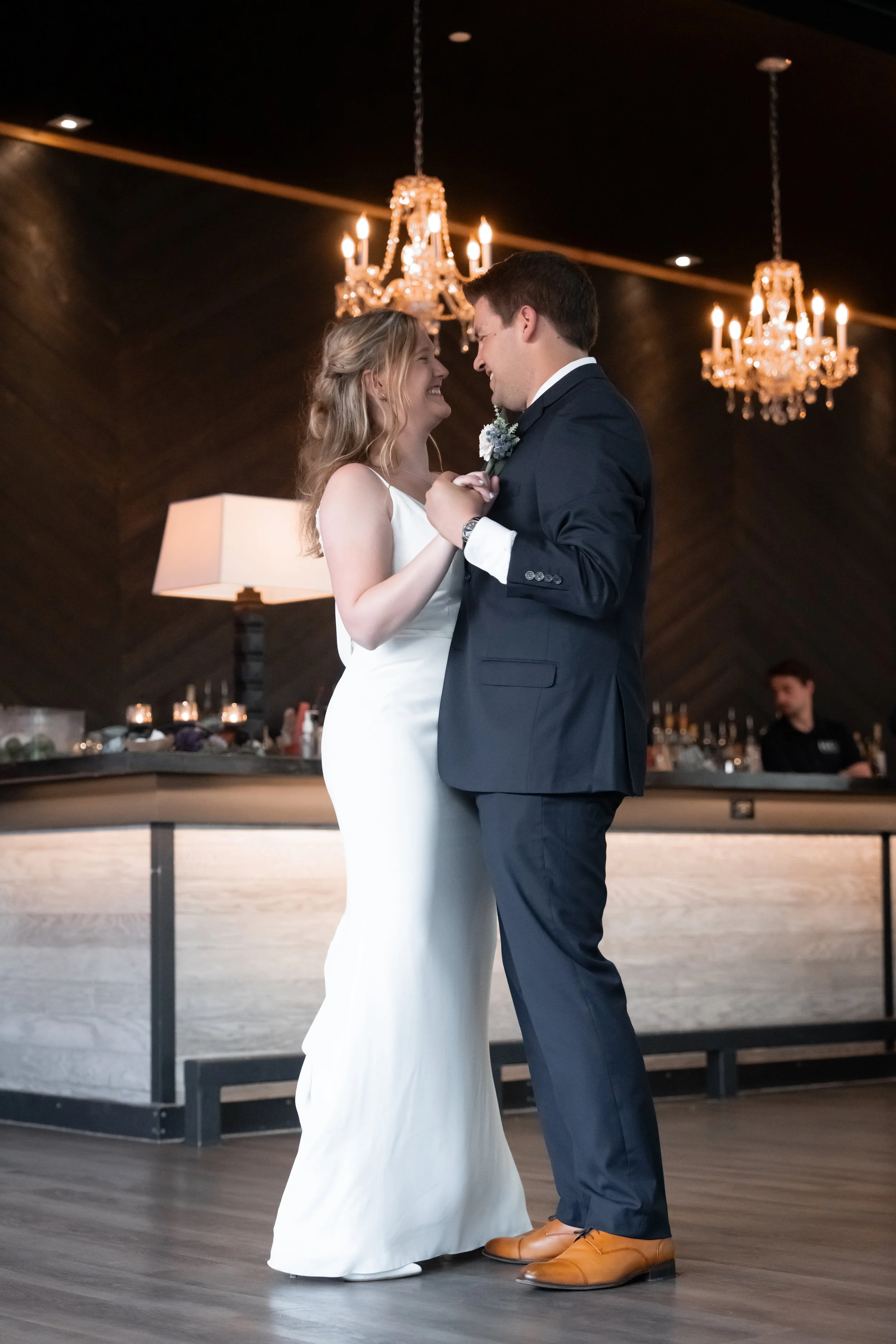 A bride and groom dancing closely at a wedding reception, with chandeliers and elegant decor in the background.