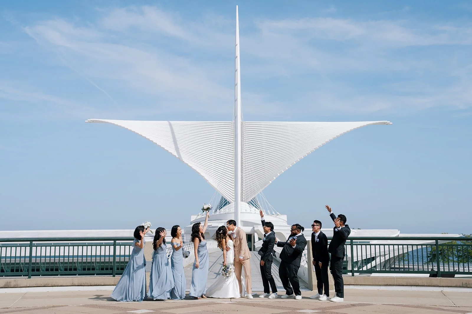 A wedding ceremony taking place outdoors on a balcony with a modern white architectural building in the background and a blue sky.