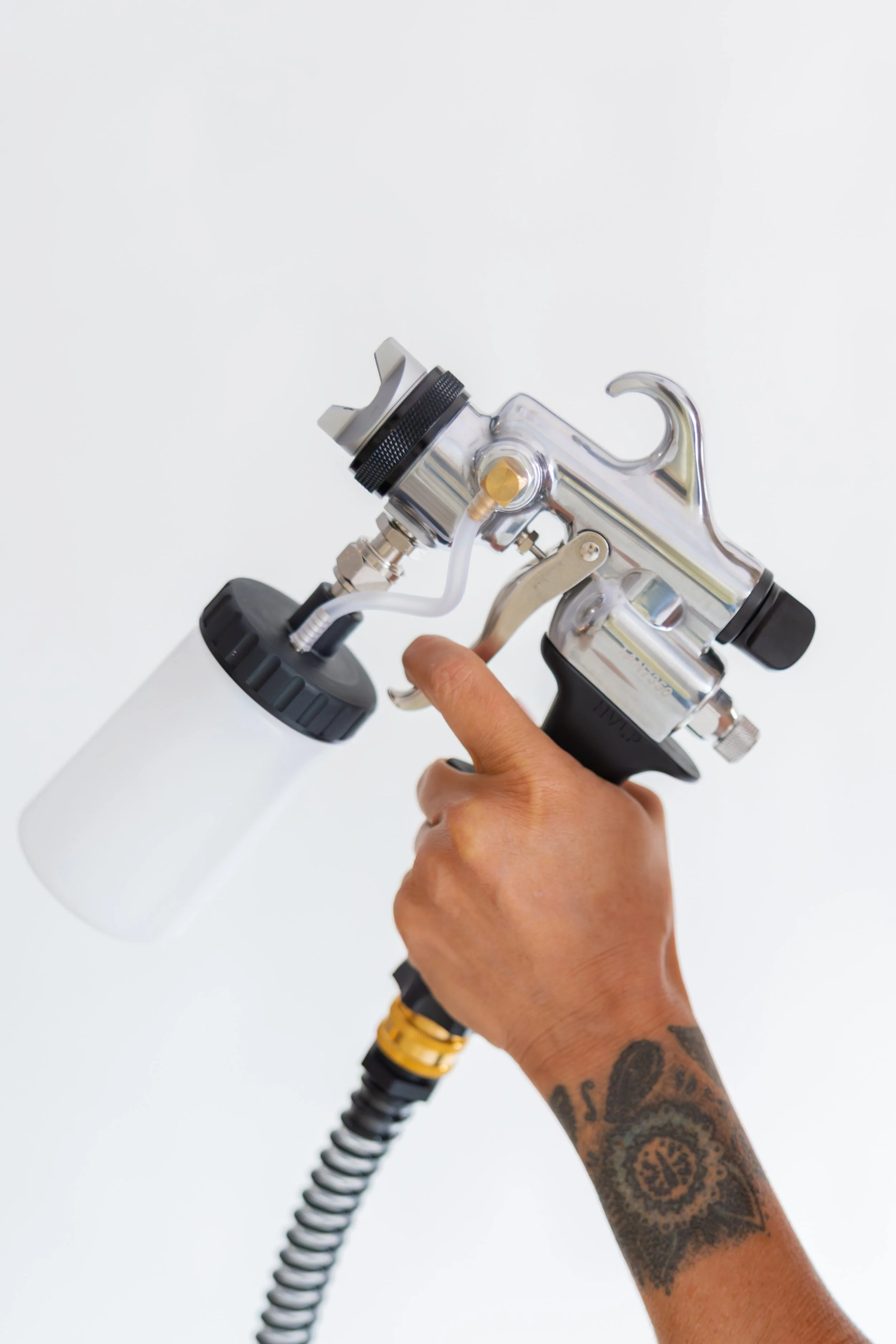 A person with tattoos on their arm holding a spray tan machine which is used for custom spray tans..
