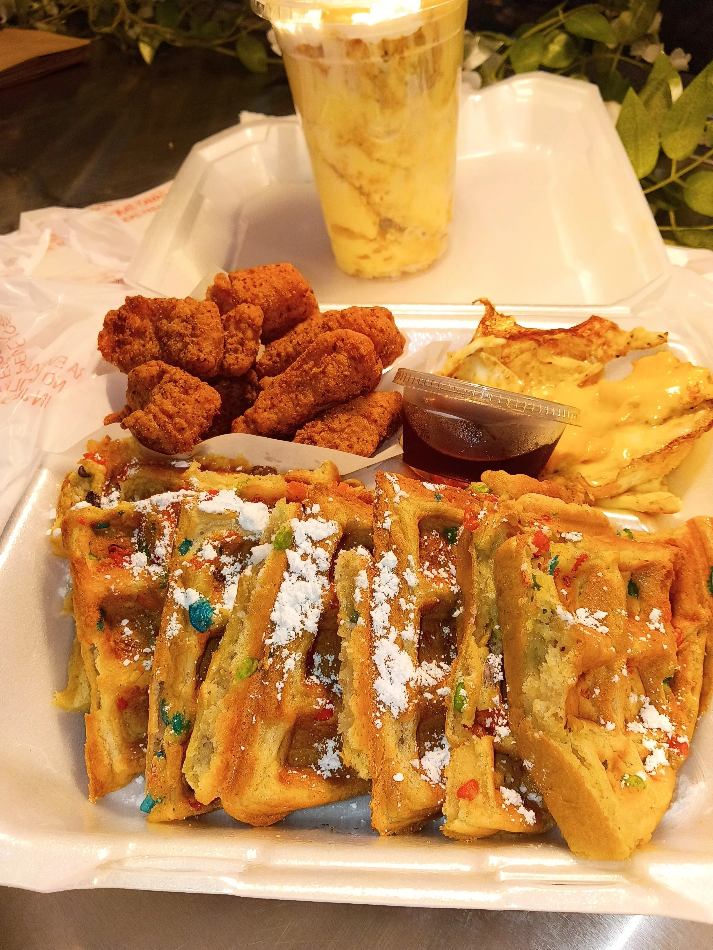 Fried chicken pieces, fried mozzarella sticks, two pieces of fried cheese, and a cheesy breadstick, with a container of dipping sauce and a drink in a plastic cup on a tray.