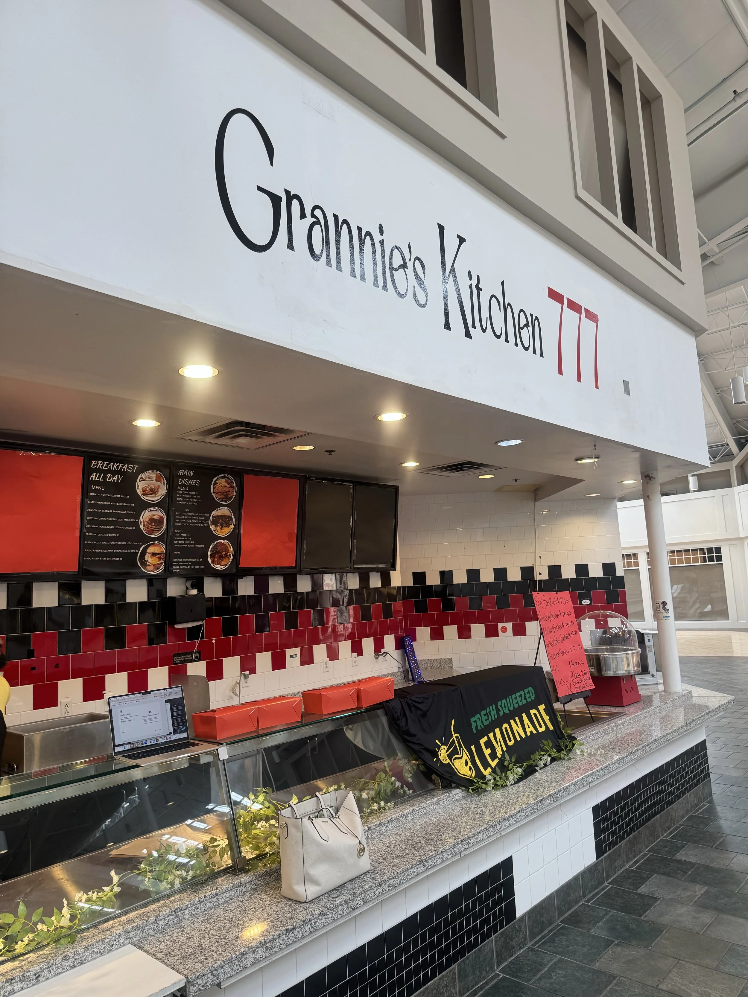 Food counter at a mall or food court with a sign reading 'Grammies Kitchen 77' and a menu board with various food options.