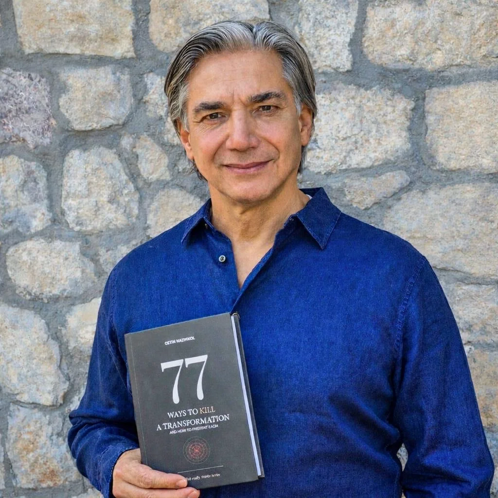 Ein Mann mit grauem Haar und blauer Hemd hält ein Buch mit dem Titel "77 Ways to Kill a Transformation" vor einer Steinmauer.