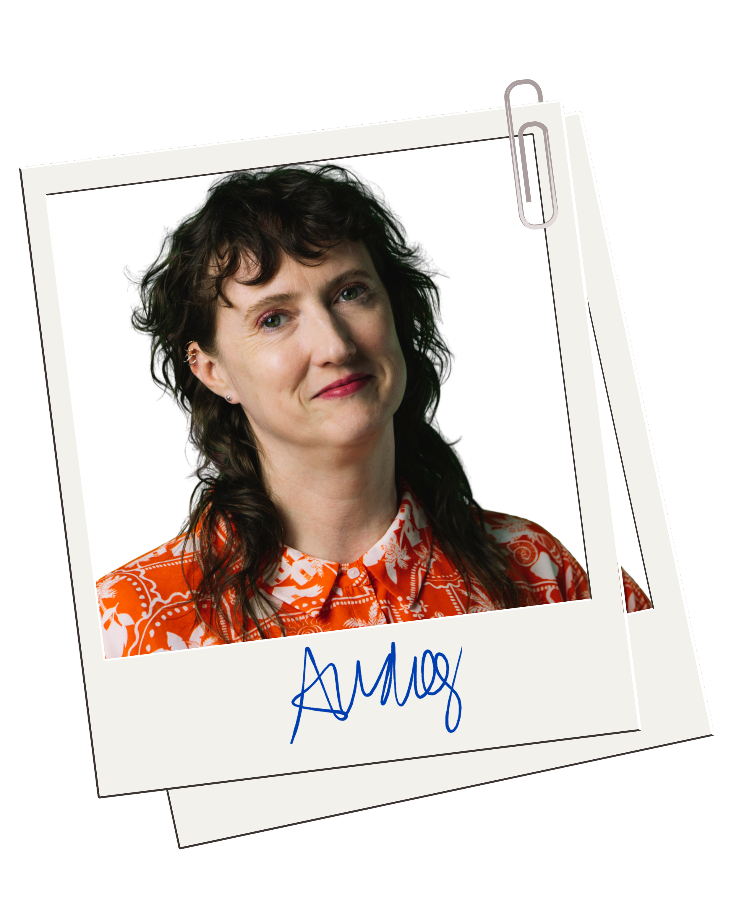 A Polaroid photograph of a woman with short curly dark hair, wearing an orange patterned shirt, smiling slightly, with a white background, and a handwritten blue signature that reads 'Audrey.'