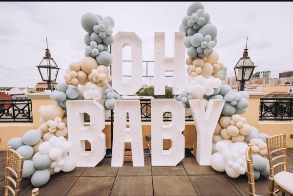 Decorative balloon arch with large white letters spelling 'OH BABY' on a rooftop terrace.