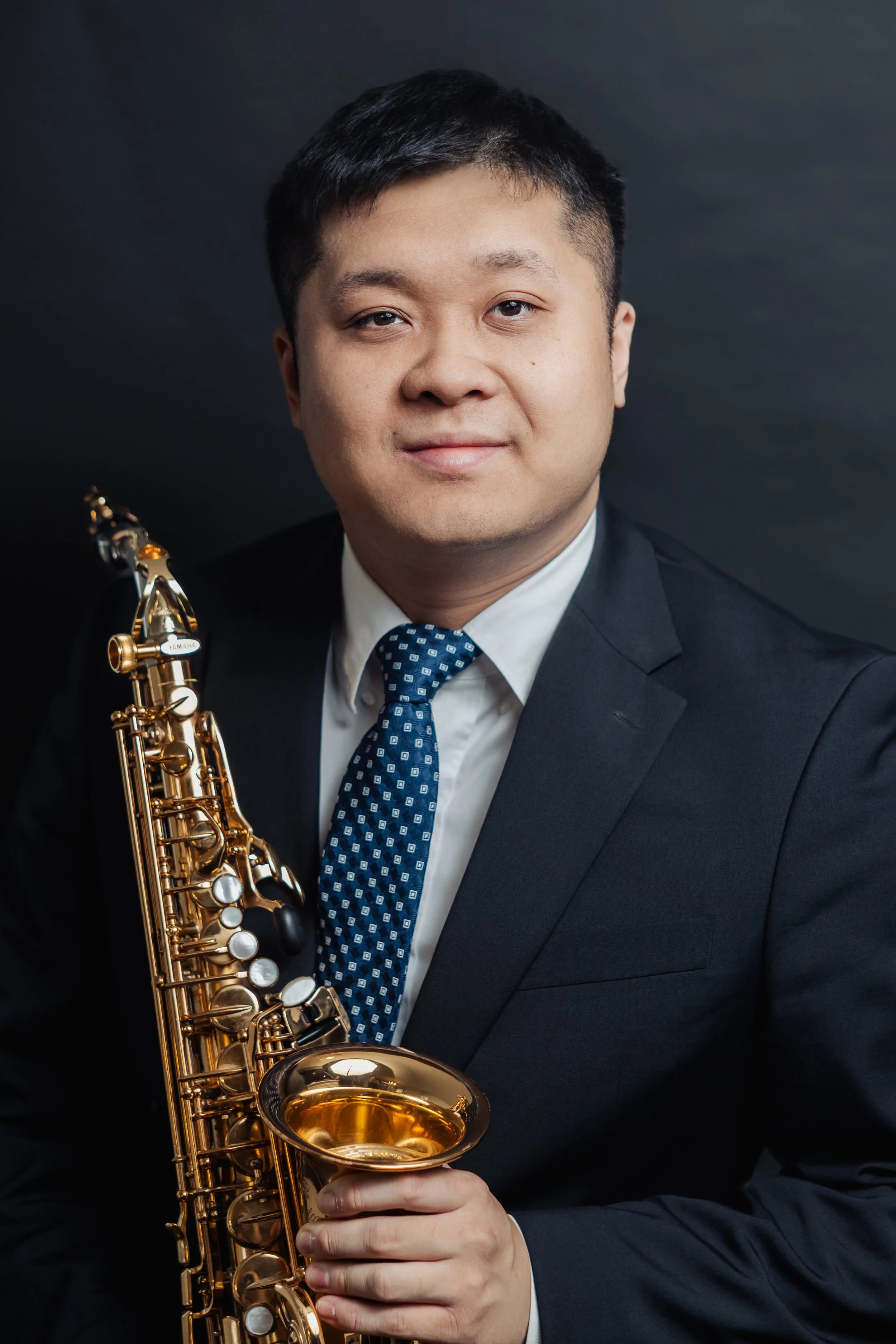 A man in a suit holding a gold saxophone against a dark background.