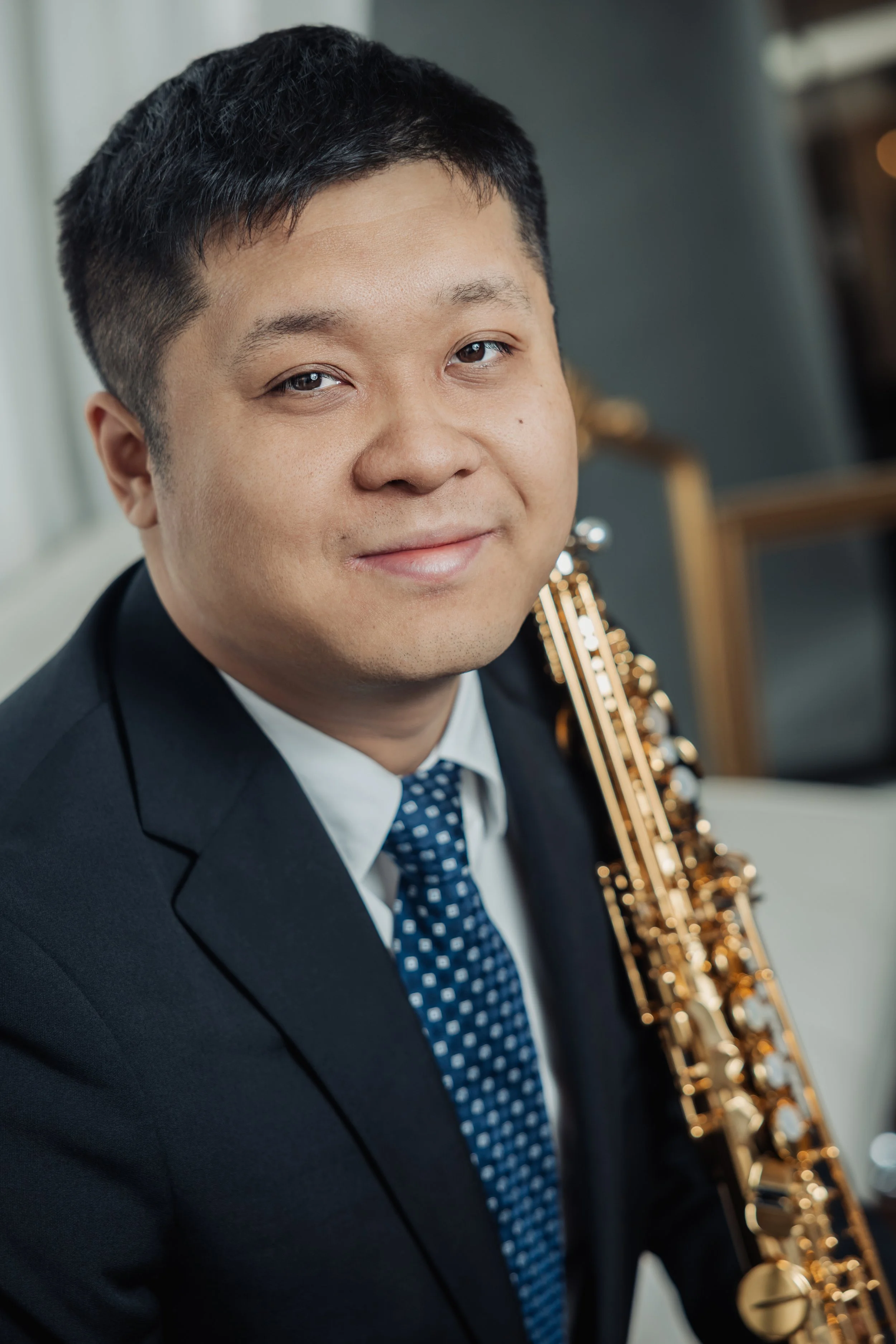 A man in a suit and tie smiling with a gold saxophone in the background.