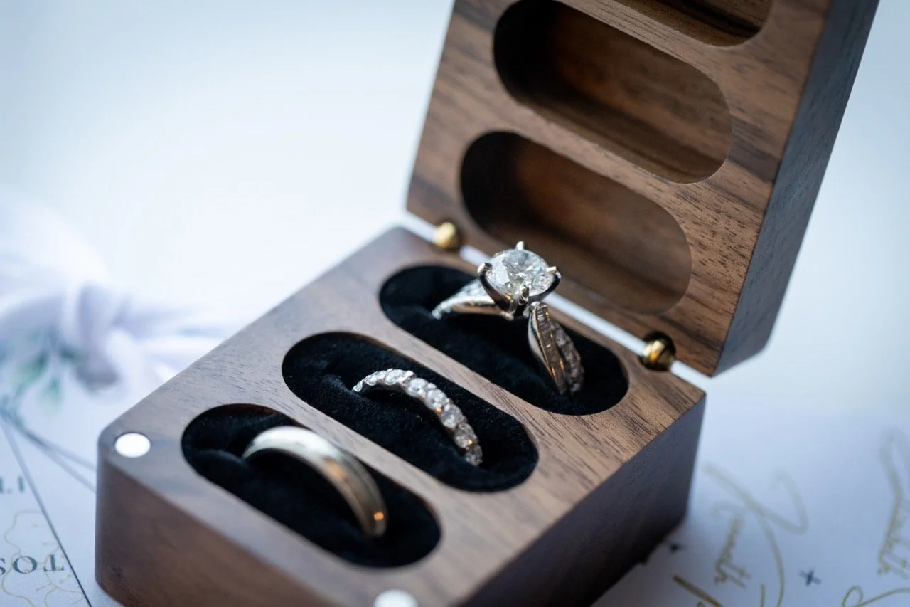 A wooden jewelry box containing three rings, including a diamond engagement ring, a wedding band, and another ring with smaller stones. This is an example of a wedding details shot in Colorado.