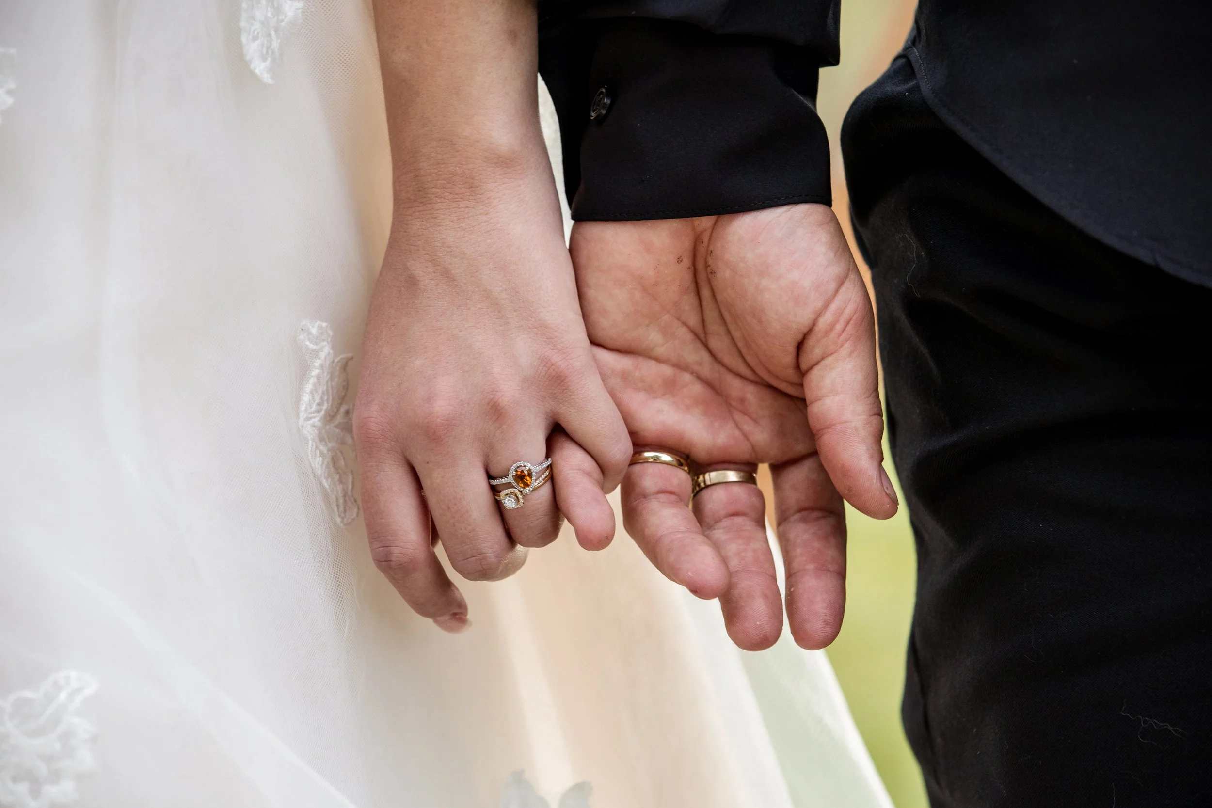 Close-up of a couple holding hands during their wedding, showing wedding rings and the woman's wedding dress.