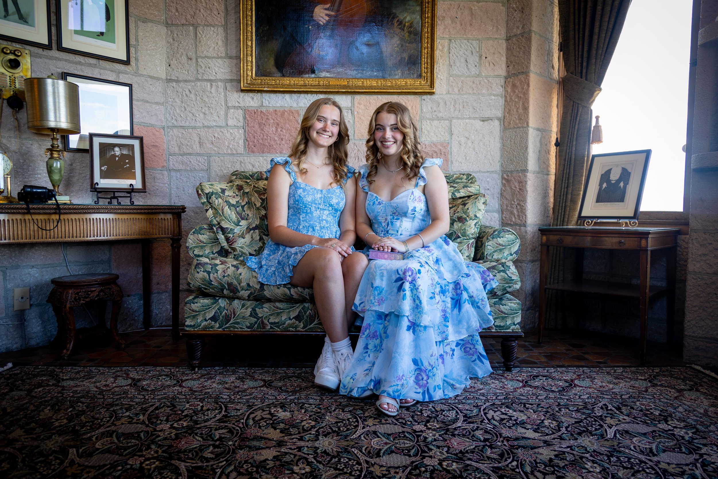 Two sisters are posed on a couch in the churchill room of the cherokee castle in Colorado. It shows the best senior portrait location in Colorado