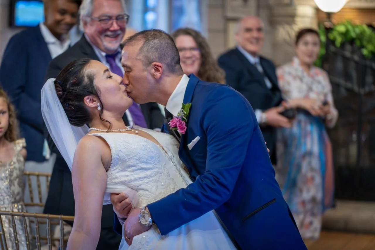 A bride and groom sharing a kiss at their wedding, surrounded by smiling guests. This is an example of candid wedding photography in Colorado.